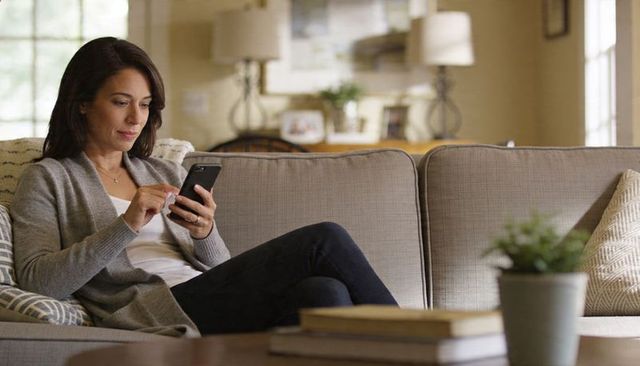 Woman relaxing on sofa using smartphone in cozy living room with neutral decor