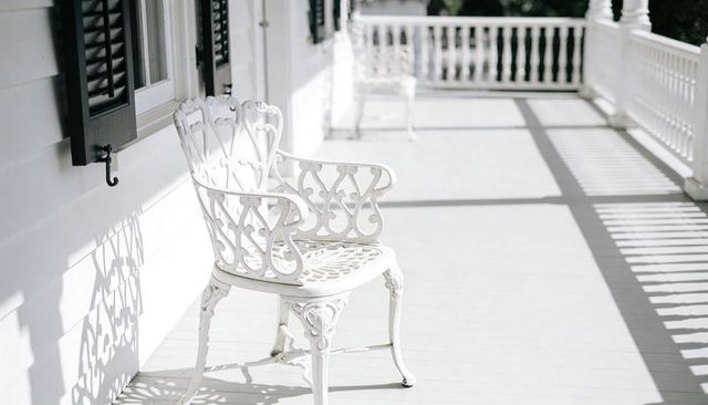 Sunlit southern porch featuring ornate white cast-iron chair and long shadow lines