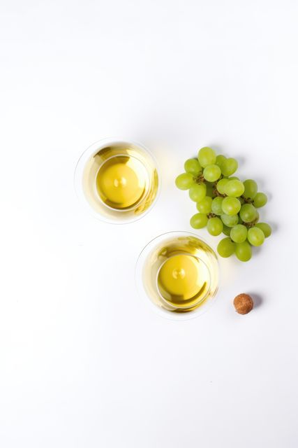 Two glasses of white wine are placed next to a bunch of green grapes on a white background. This minimalist and elegant composition is ideal for use in food and beverage promotions, wine tasting event advertisements, and articles on wine pairing. The bright and clean aesthetic also makes it suitable for culinary blogs, restaurant websites, and social media posts related to luxurious dining experiences.