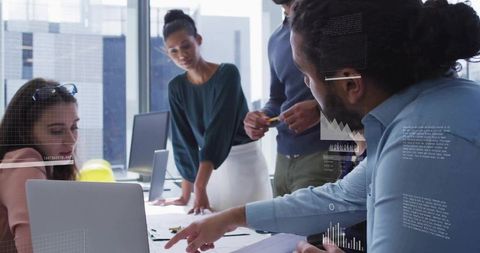 Diverse team collaborating around laptop in modern glass office with data overlays