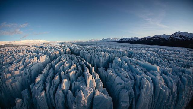 Jagged glacier seracs and deep crevasses stretching across alpine ice valley at dawn