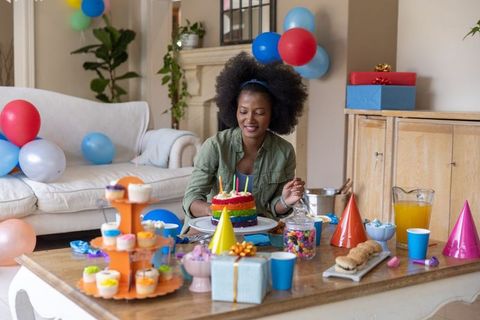 African american woman blowing candles on rainbow birthday cake at cozy home celebration