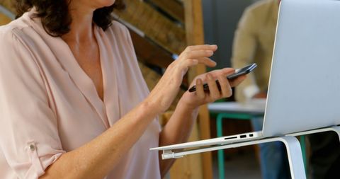 Businesswoman in Modern Office Multitasking with Laptop and Smartphone
