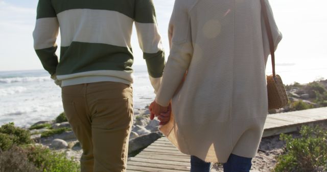 Rear midsection of senior caucasian couple holding hands walking on sunny coastal path. Togetherness, relationship, romance, retirement, vacations, wellbeing and active senior lifestyle, unaltered.