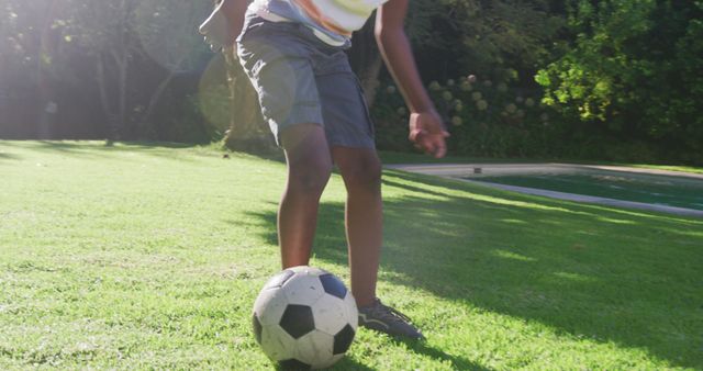 This image shows a child engaging in outdoor play by kicking a soccer ball in a sunny garden. Great for illustrating healthy outdoor activities, children's sports, and summer fun. Ideal for use in advertisements, blogs, and articles related to youth sports, outdoor play, and active lifestyles.