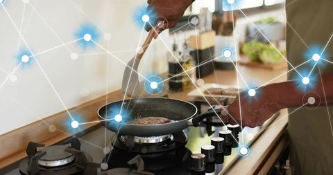 Senior flipping burger on gas stove with digital smart kitchen network overlay, skillet