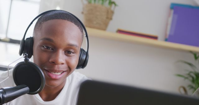 Young African American male podcaster engaging with audience, recording from home with professional microphone and headphones. Ideal for content related to technology, podcasting, home studios, or youth engagement in media. Perfect for illustrating online content creation in a professional yet relatable setting.