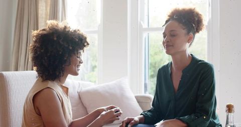 Presenting gift on sofa, woman sharing surprise with friend in bright cozy living room
