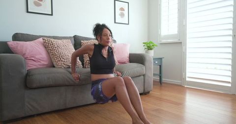 African american woman performing triceps dips on sofa in sunlit modern living room