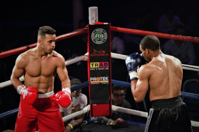 Two professional boxers are competing in a high-energy boxing match inside the boxing ring. The focus is on their muscular physiques and the determination in their expressions. This image is suitable for use in articles about sports, fitness programs, athlete training, boxing events, and motivational sports content.