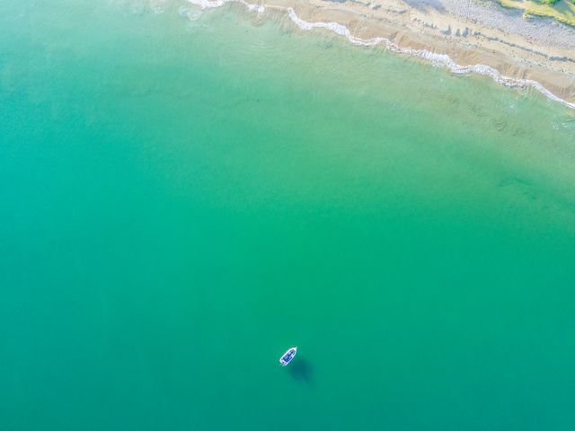Overhead view showcasing a boat on tranquil emerald green water near a sandy beach. Useful for travel brochures, holiday planners, tourism advertisements, websites promoting coastal destinations, or serene nature scenes.