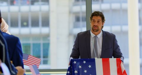 Business Seminar Speaker Addressing Enthusiastic Audience with American Flags