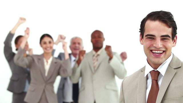 Businessman confidently smiling in front with diverse team cheering in background. Highlights supportive team atmosphere and collective success. Perfect for promoting workplace positivity, team building, corporate success stories, empowerment in business settings, and motivational materials.