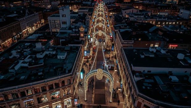 Evening shopping avenue glowing with arched festive lights and strolling winter shoppers