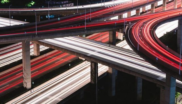 Nighttime multi-level highway interchange with sweeping red and white light trails