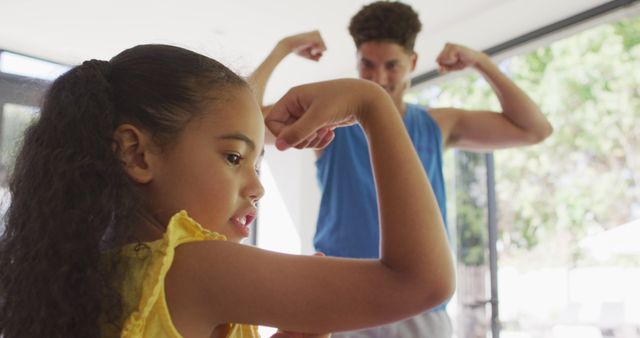 Father and daughter enthusiastically showing their muscles in a well-lit living room. Perfect for illustrating family bonding, strength, happiness, or playful moments at home. Ideal for use in advertisements promoting family fitness, healthy lifestyles, or familial relationships.