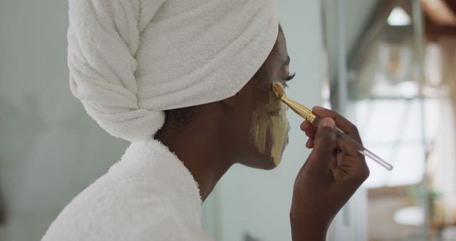 Portrait of african american attractive woman applying face mask in bathroom. beauty, pampering, home spa and wellbeing concept.