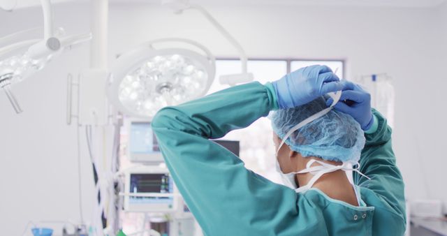 Surgeon adjusting surgical cap and gloves before performing a medical procedure in a brightly lit operating room. Useful for medical and healthcare-themed materials, showcasing medical professionals in sterile environments, and demonstrating preparation steps before surgery.