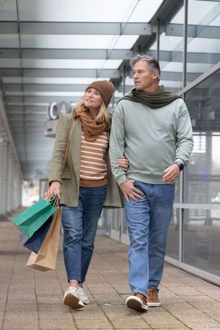 Middle-aged couple walking arm-in-arm carrying shopping bags by glass storefront