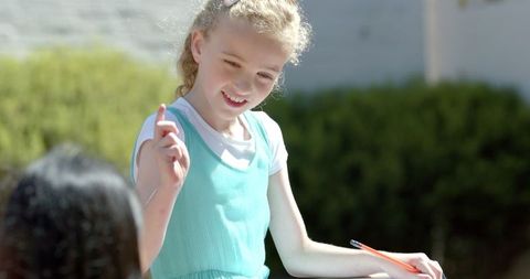 Blonde girl drawing outdoors in schoolyard in blue dress