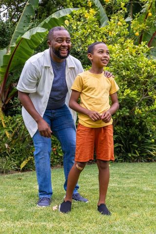African american father guiding smiling son near lemon tree in tropical backyard