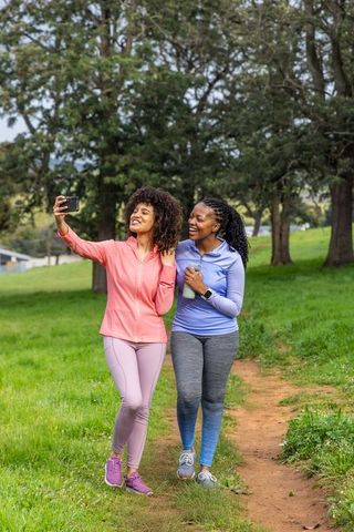Diverse women walking and taking selfie on park trail in colorful activewear