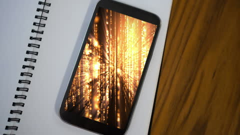 Smartphone Displaying Orange Data Streams on Notebook