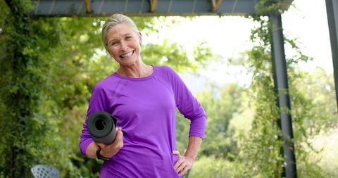 Elderly woman holding yoga mat ready for outdoor exercise