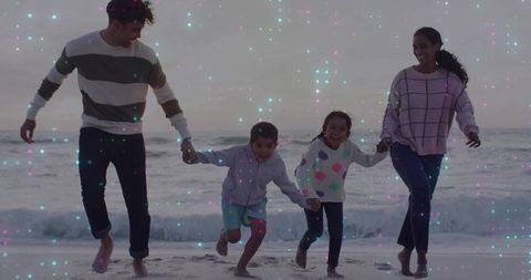 Family of four running and holding hands on wet sand beach wearing sweaters with pastel sparkles