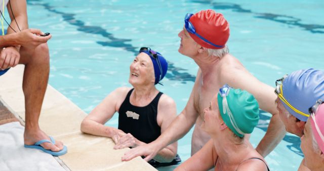 Group of elderly men and women in swim caps listening attentively to a coach by pool edge. Useful for depicting senior health, fitness programs, aqua aerobics classes, community activities for older adults, and promoting active lifestyles among senior citizens.