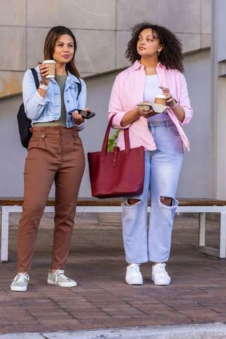 African american female friends holding coffee and snack while chatting outdoors