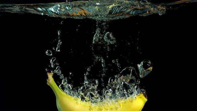 Banana creating dramatic splash as it falls into clear water against black background. Ideal for use in food and beverage advertisements, health and nutrition promotions, or as vibrant visual content for blogs and social media campaigns.