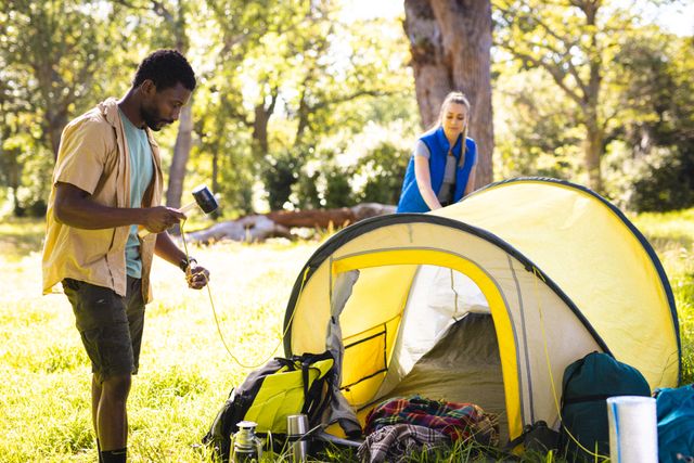 Diverse couple preparing tent in park on sunny day. Spending quality time, lifestyle and camping concept.
