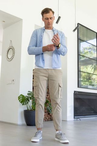 Man adjusting wristwatch in modern living room wearing blue shirt and beige cargo pants