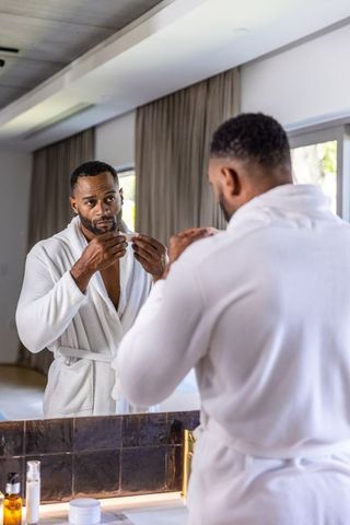 Mature african american man flossing teeth at luxury bathroom vanity wearing white robe