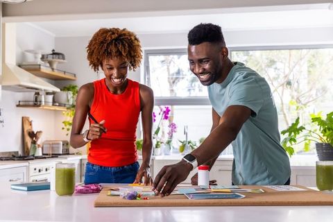 African american couple creating corkboard vision board together in sunlit modern kitchen