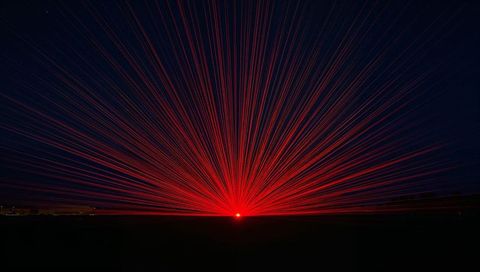Radiating Red Starburst Laser Beams Over Dark Horizon Casting Radial Light Across Field