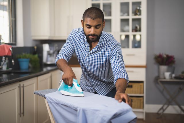 Young man ironing cloth in domestic kitchen at home