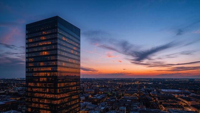 Glass tower reflecting sunset over illuminated city skyline at dusk
