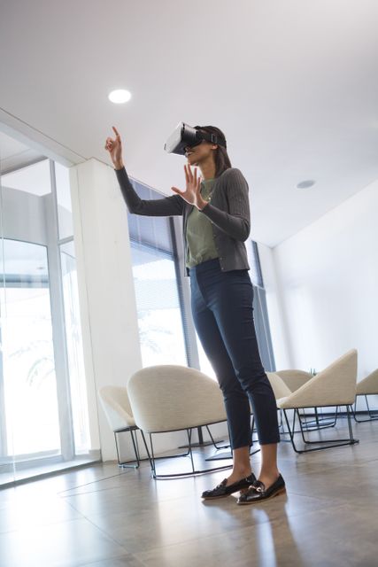 A businesswoman uses a virtual reality headset in a modern office environment, indicating the integration of advanced technology in corporate settings. This image is ideal for illustrating concepts related to futuristic workplaces, innovation in business, and the use of cutting-edge technology in professional environments.