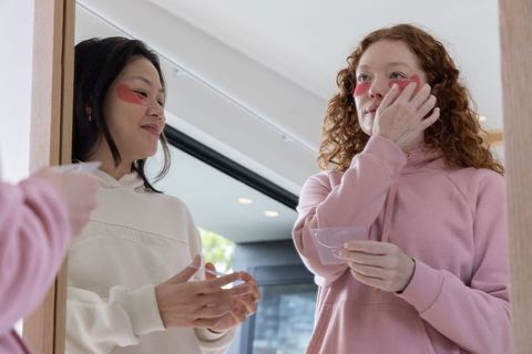 Friends applying under-eye gel patches at vanity sharing cozy skincare routine in home