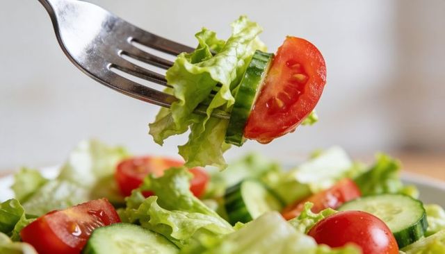Fork lifting fresh salad bite with crisp lettuce cherry tomato and cucumber