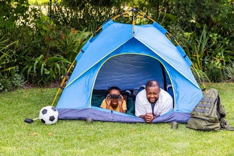 African american father and son camping in backyard tent bonding over binoculars
