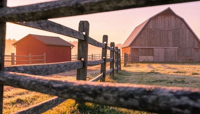 Weathered split-rail fence leading to gambrel barn at sunrise on rural farm with dew glow