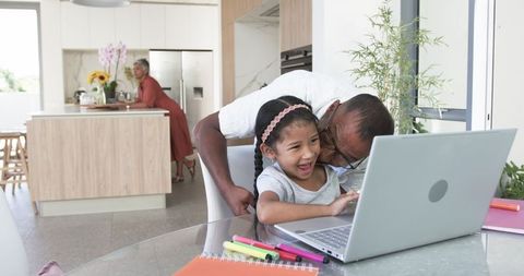 Grandfather Helping Granddaughter with Laptop in Modern Kitchen