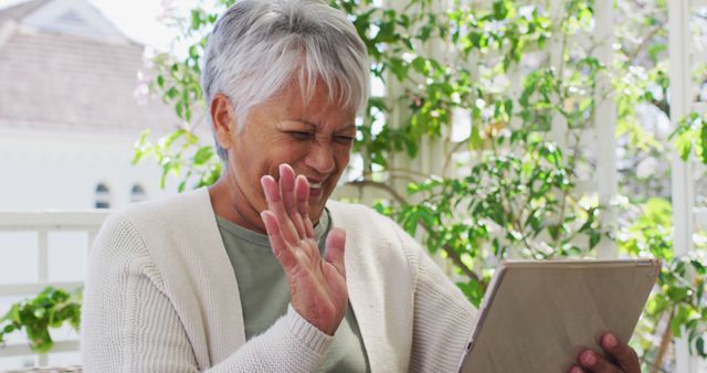 Senior biracial woman having image chat using tablet in garden. blowing kisses. self isolation retirement lifestyle at home during coronavirus covid 19 pandemic.