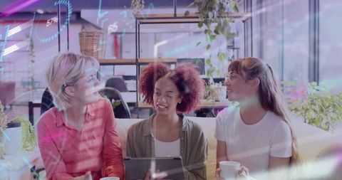 Women collaborating in modern coworking lounge holding tablet and coffee, creative teamwork