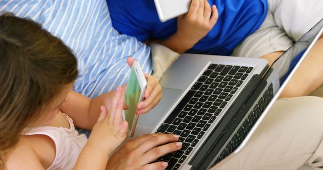 Children using digital devices like laptop, smartphone, and tablet at home. Great for content related to modern family, technology, digital natives, online learning, and parent-child interaction.