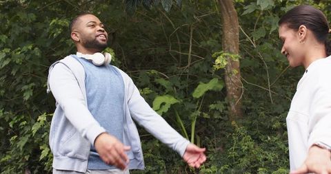 Young friends greeting and embracing in wooded park with headphones and casual clothing