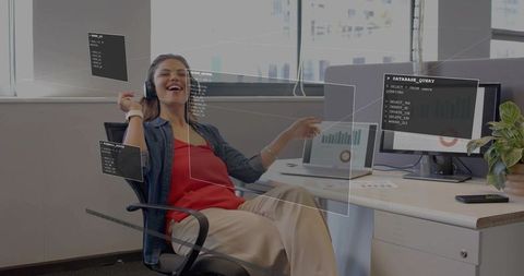 Woman enjoying music while interacting with holographic data dashboards at office workstation